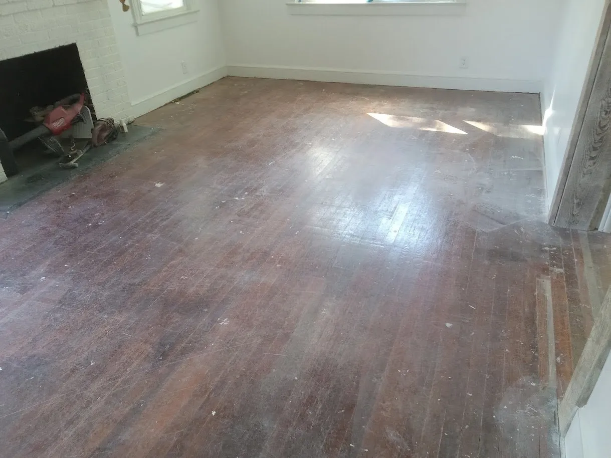 Worn cherry-red stained floor in a room with a brick fireplace before refinishing